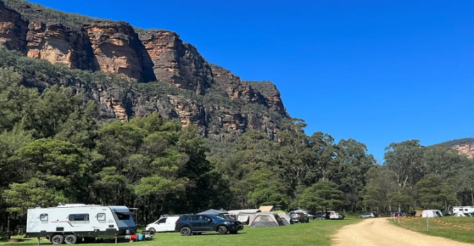 Coorongooba campground with tents caravans and cars surrounded by the majestic cliffs of the eastern end of the Capertee valley.