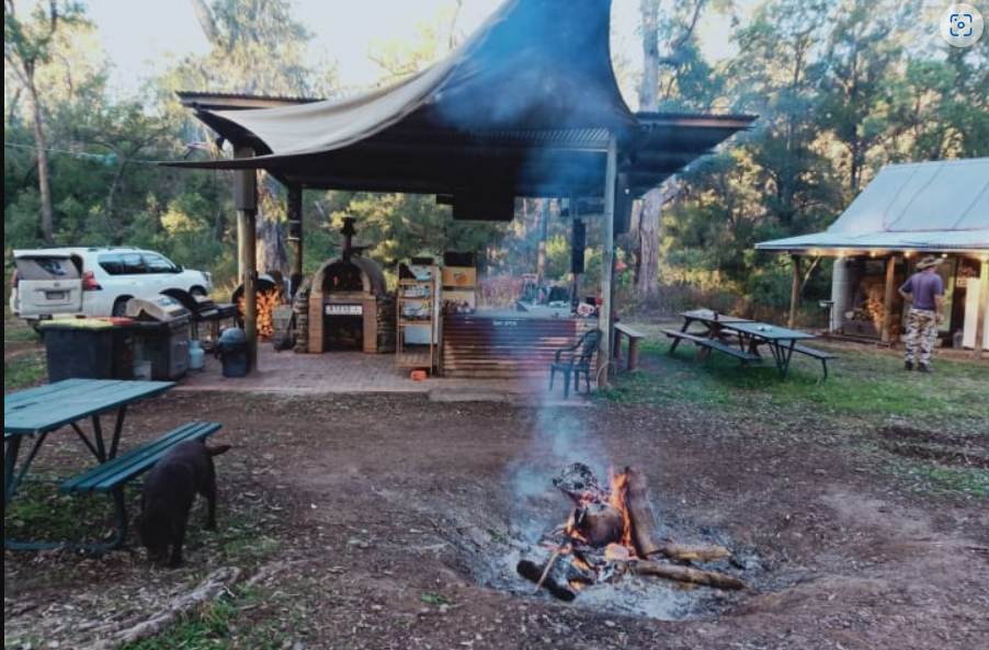 Dalli's campground with building right hand side, motor vehicle next to sheltered seating in the middle with fire and seating in foreground.